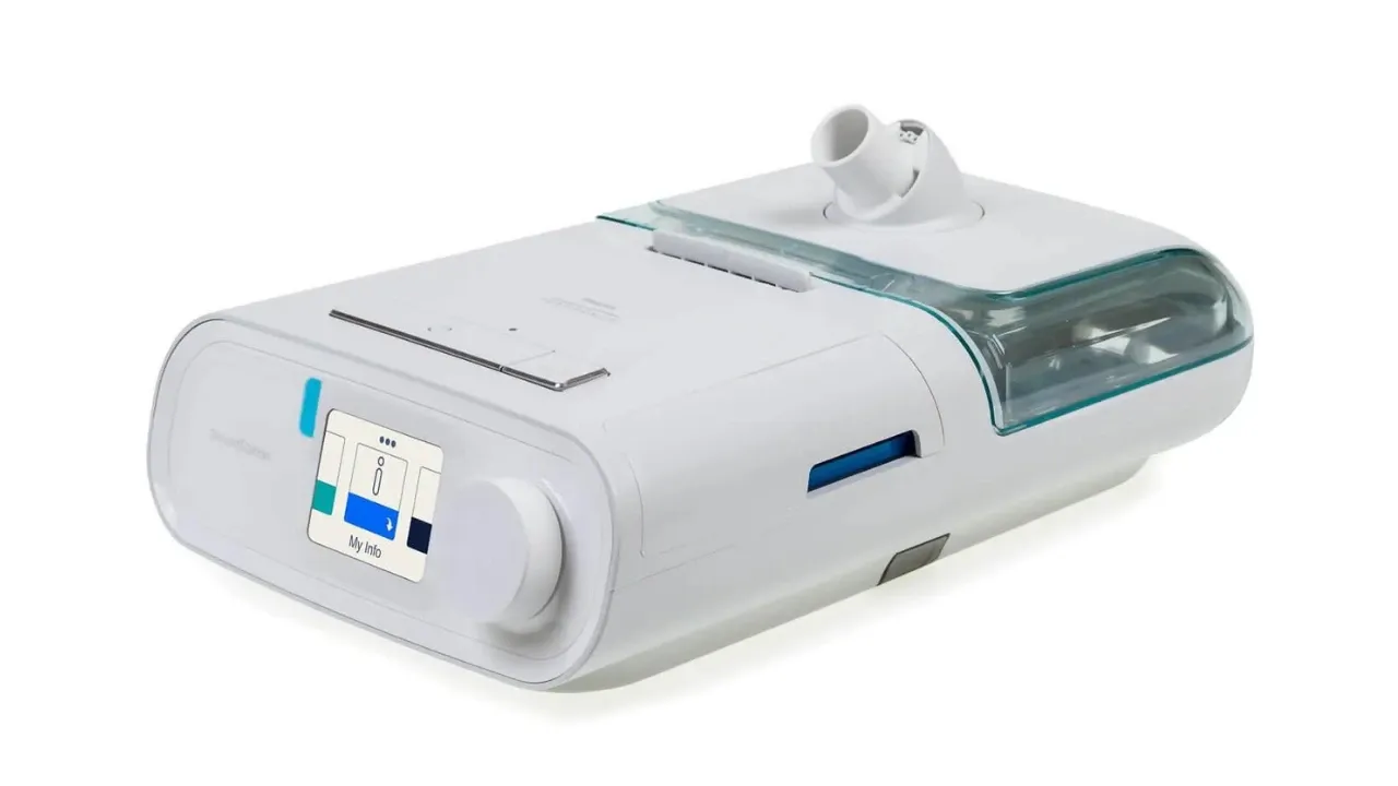 Aparelho de CPAP Philips DreamStation branco visto de três quartos, com a câmara de água do umidificador acoplada ao lado